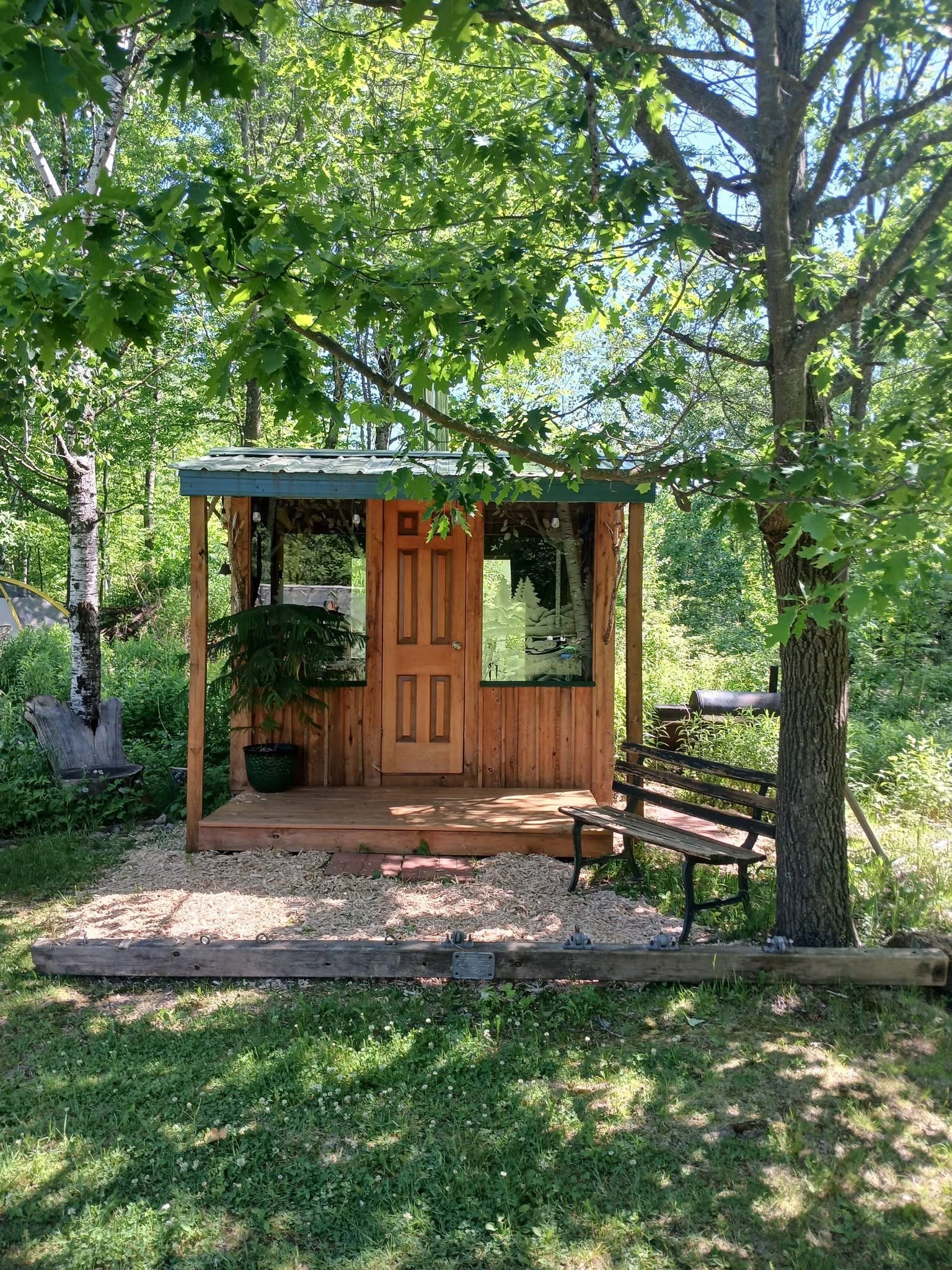 A shaded cabin porch with a bench, under the trees