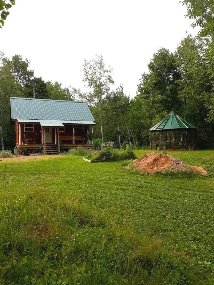 The main cabin and the round corn crib across a rough field, with a mound of fresh soil between them